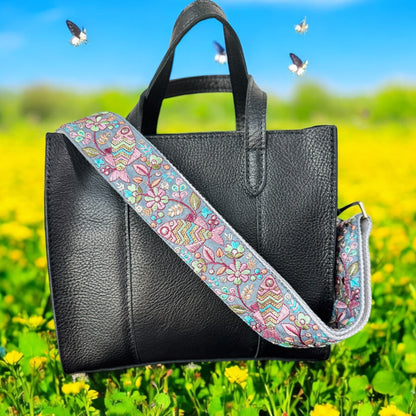 Adjustable embroidered purse strap with floral patterns and gold hardware, displayed on a gray background.