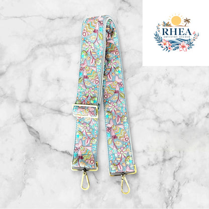 An adjustable embroidered purse strap with floral patterns and gold-colored hardware, displayed on a gray background.