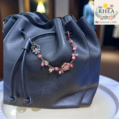 Blue leather drawstring bag with a pink beaded purse charm on a white surface, RHEA brand visible.