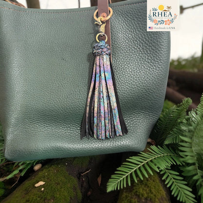 Green handbag with a colorful tassel keychain, set against a natural background.