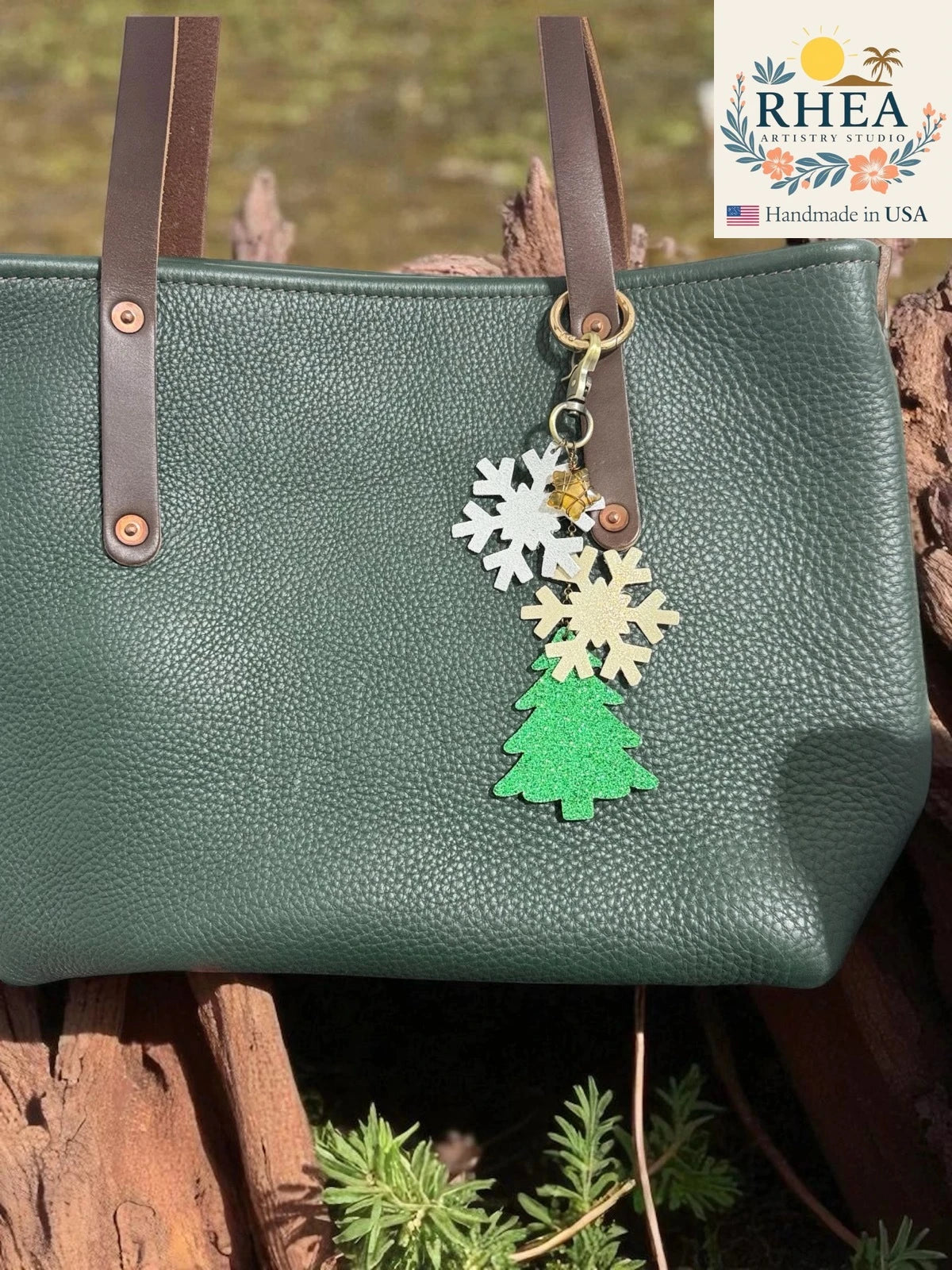 Green handbag with decorative christmas purse charm featuring a tree and snowflakes, branded 'RHEA'.