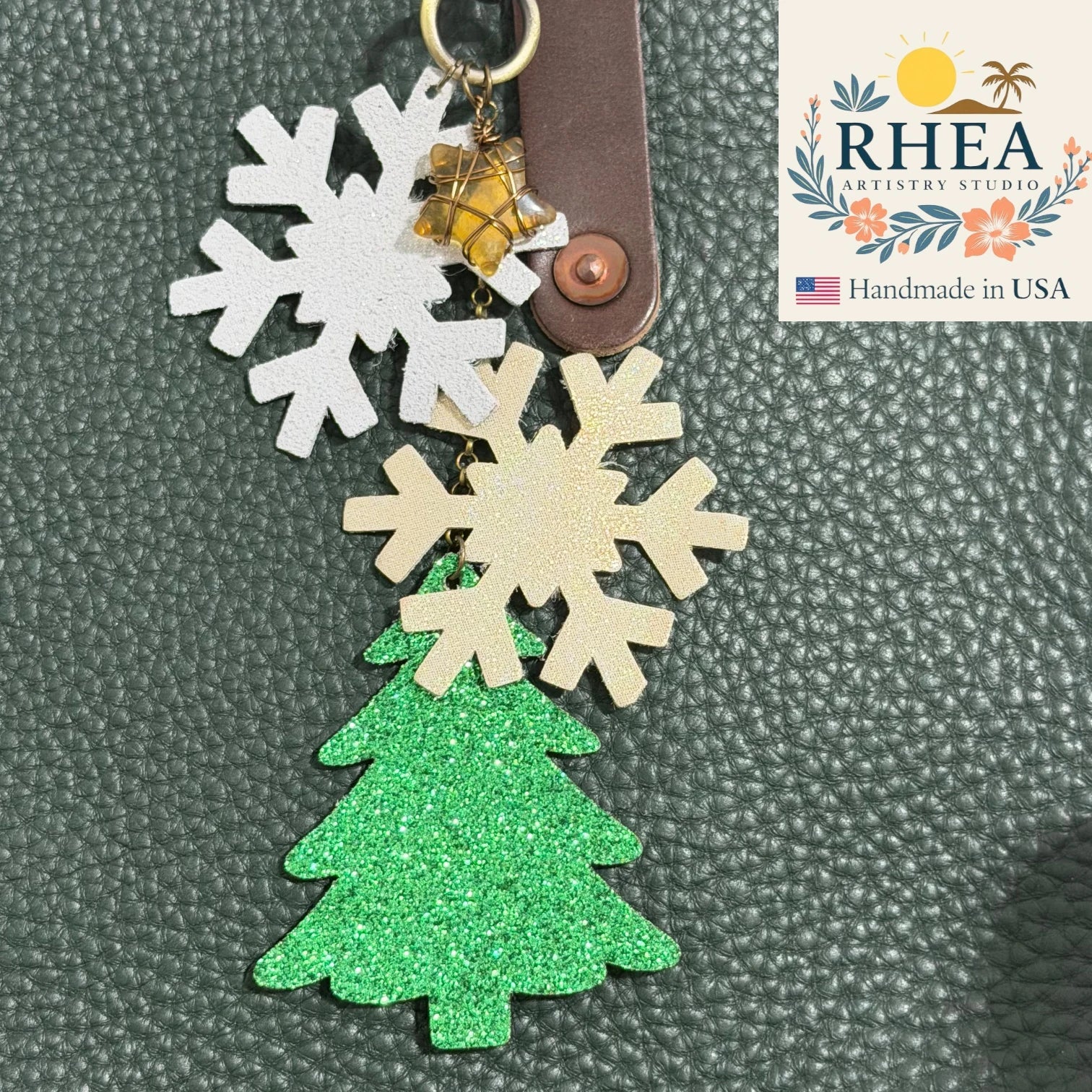 Keychain with snowflake and tree designs on a textured surface, featuring the RHEA Artisans Studios logo.