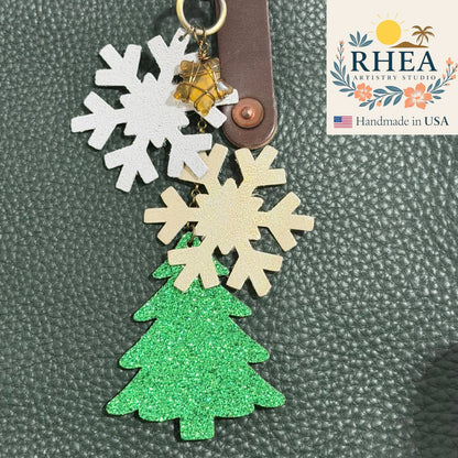 Keychain with snowflake and tree designs on a textured surface, featuring the RHEA Artisans Studios logo.