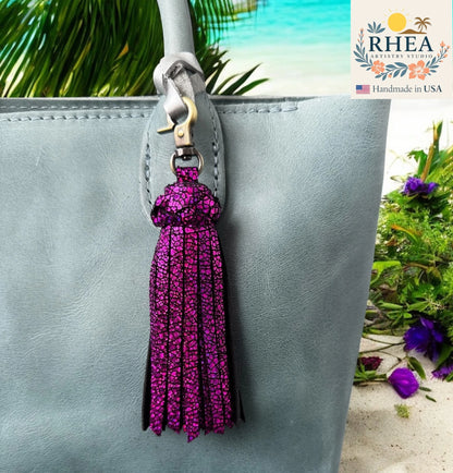 Purple tassel keychain attached to a gray bag with a blurred natural background