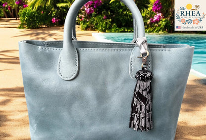 Light blue handbag with a tassel keychain by RHEA, set against a poolside background.