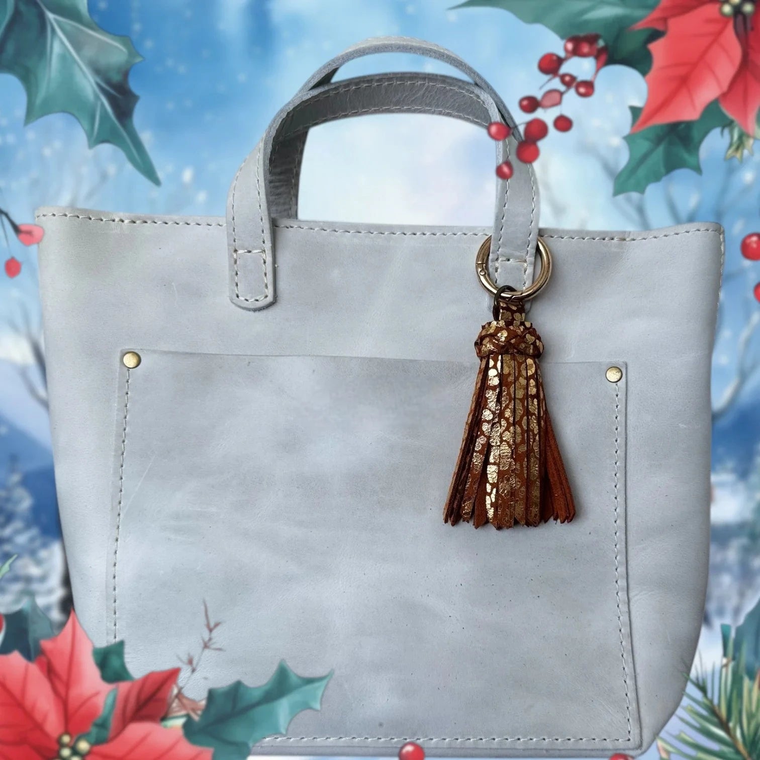 Gray handbag with a brown tassel on a decorative background with holly and berries.