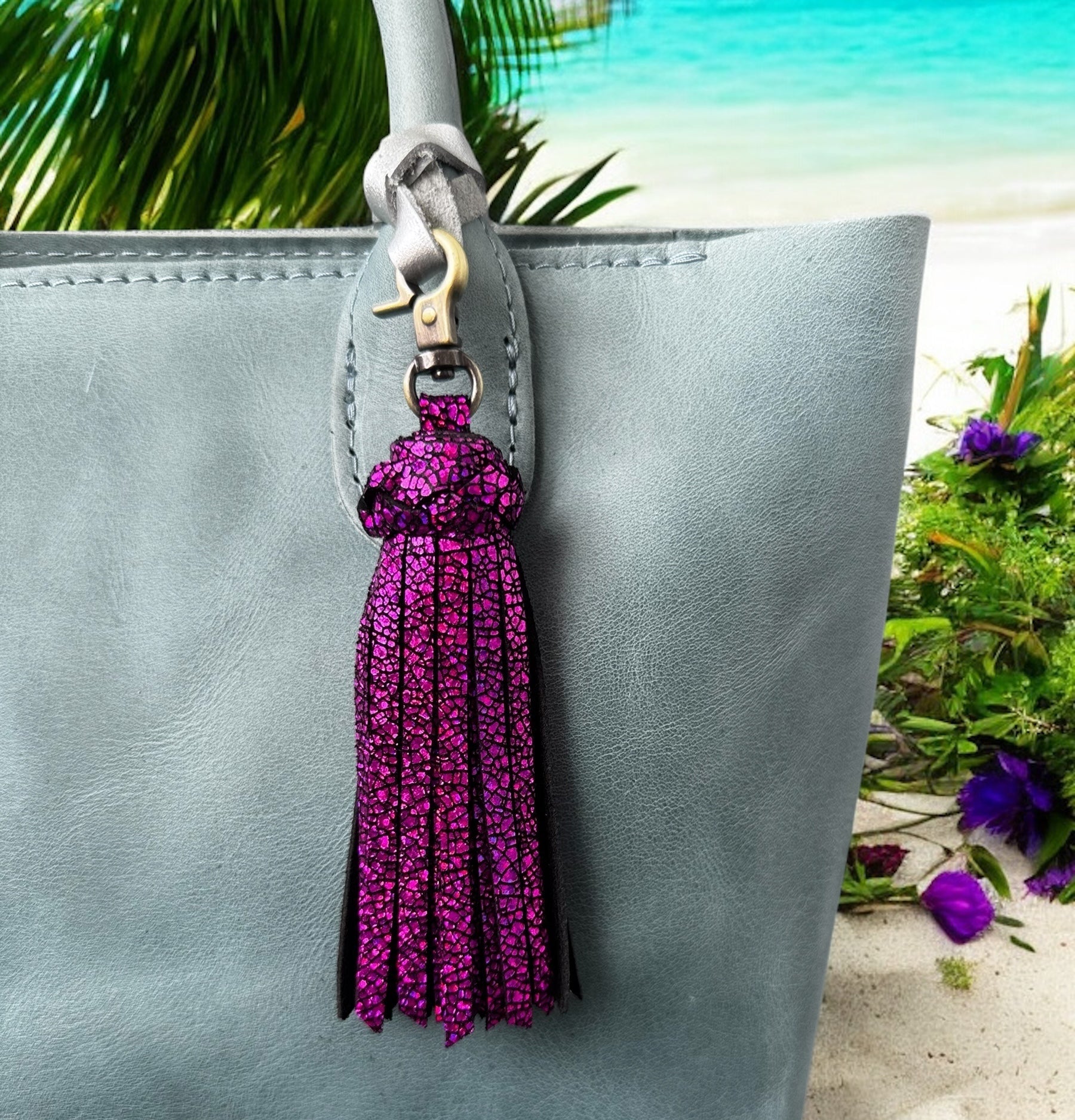 Purple tassel keychain attached to a gray handbag with a beach background
