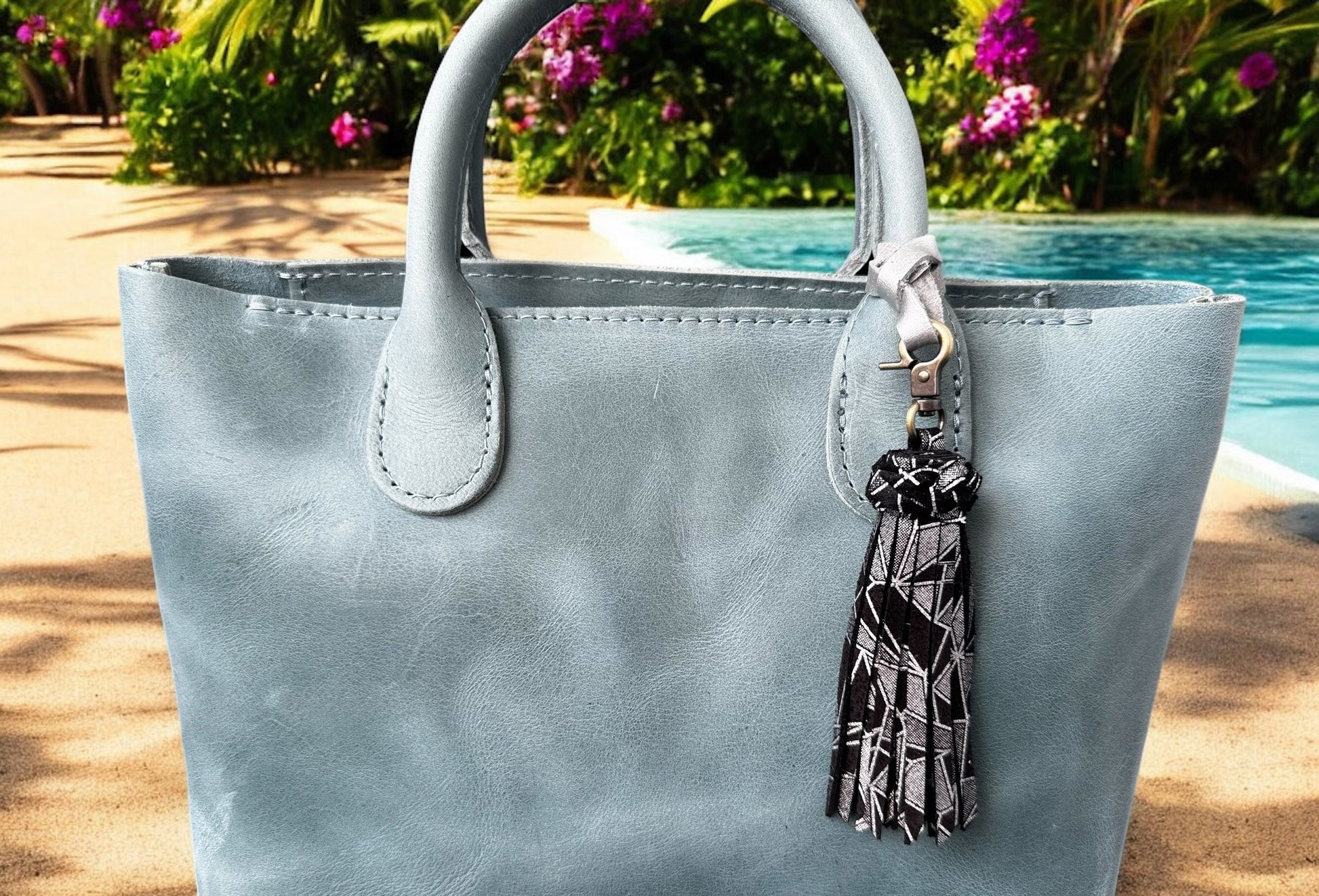 Light blue handbag with a tassel keychain by a poolside