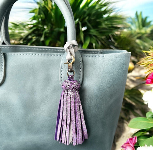 Gray handbag with a purple tassel charm against a natural background