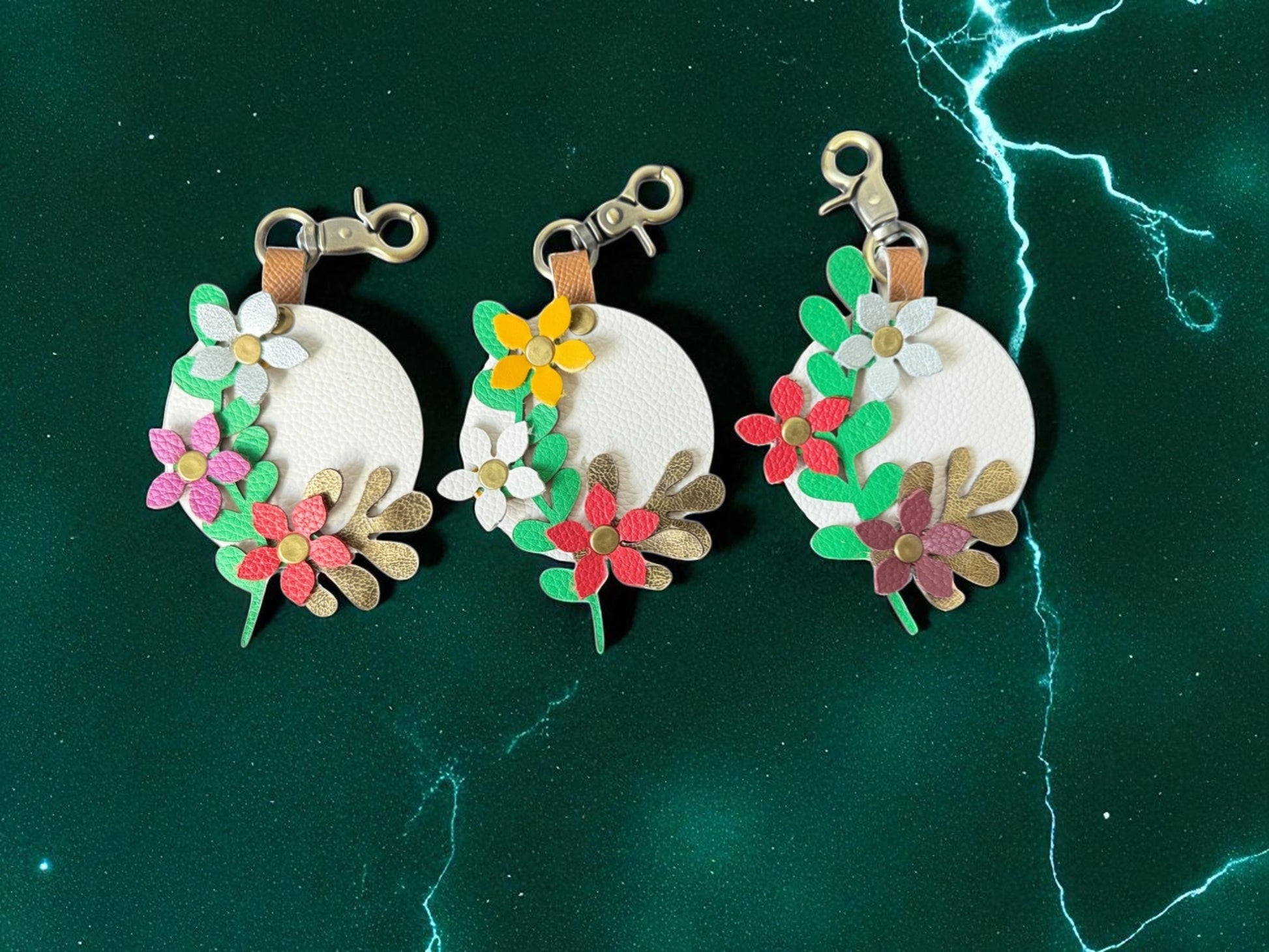 Three floral keychains on a green background with lightning effects