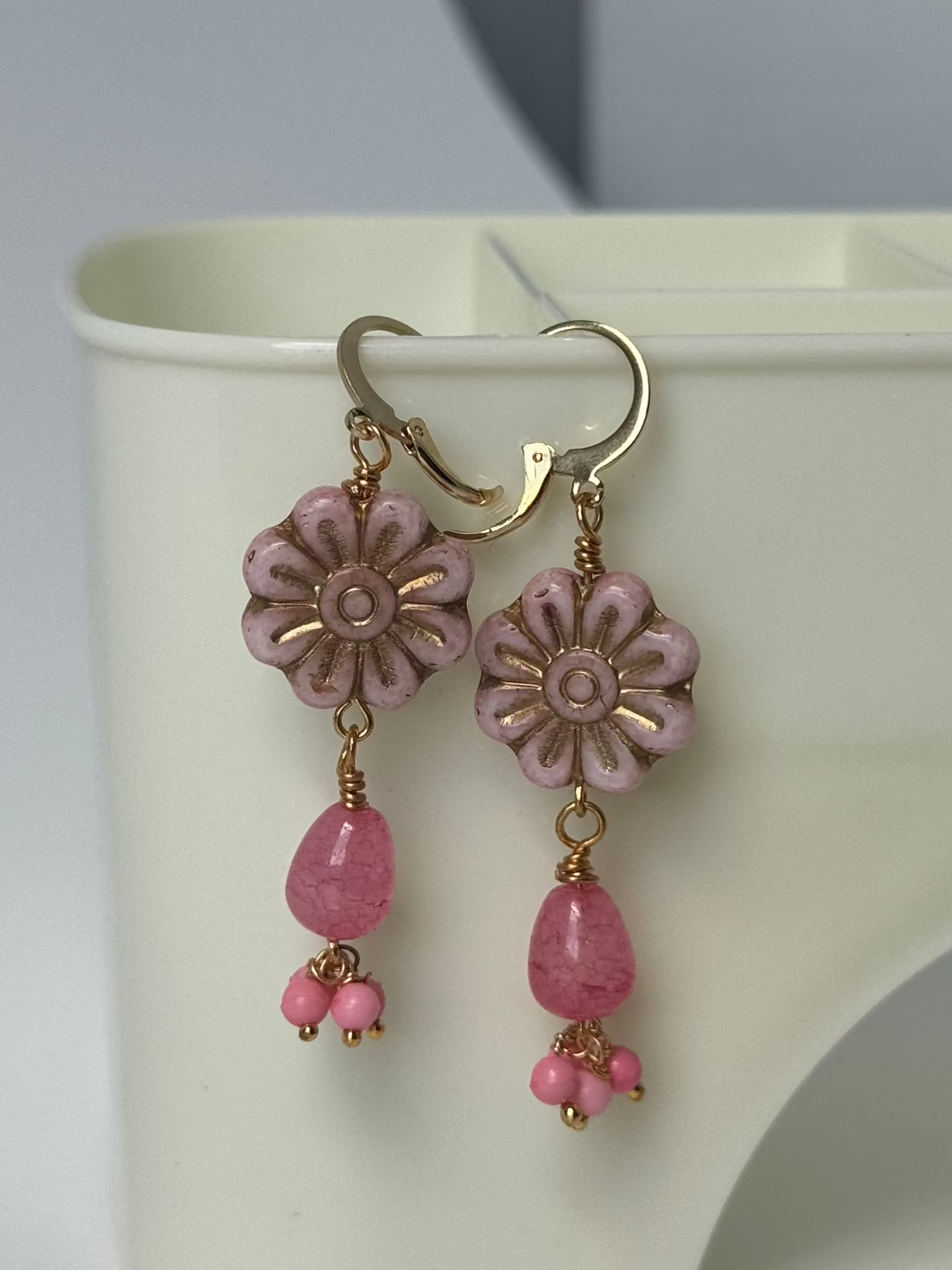 Floral earrings with pink beads on a pink background with flowers and fruits.