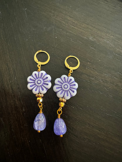 A pair of blue glass drop earrings with gold plated brass findings, displayed on a flat surface with grass and a clear sky in the background.