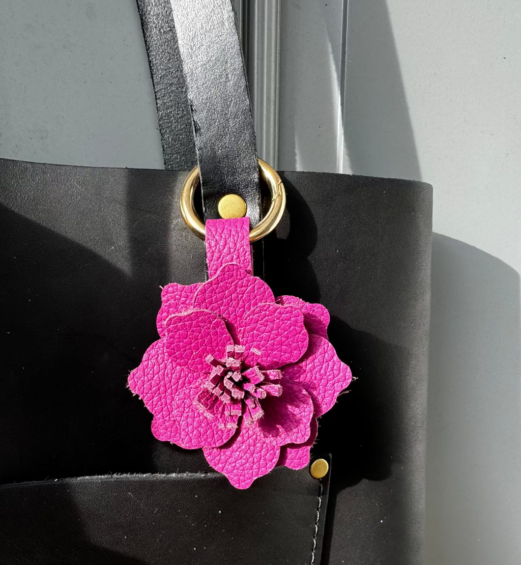 A close-up of a pink leather flower charm with a lobster clasp and split ring, designed to resemble a peacock flower.