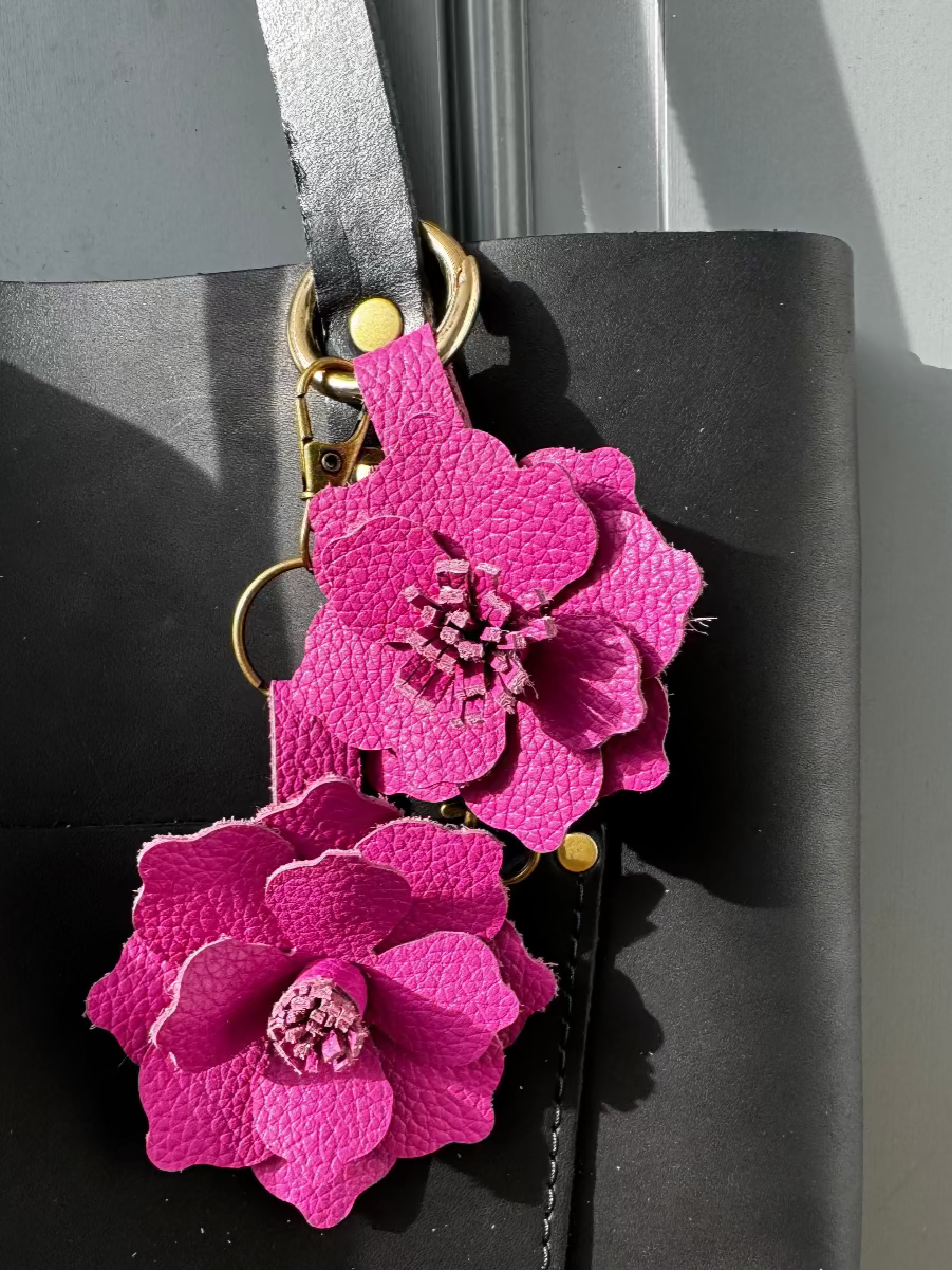 A close-up of a pink leather flower charm with a lobster clasp and split ring, designed to resemble a peacock flower.