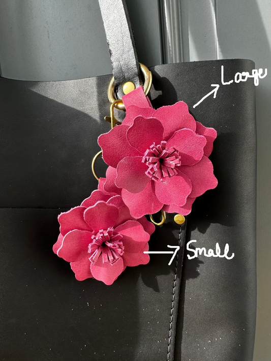 A small leather flower accessory in old rose color, attached to a black strap with a lobster clasp and a split ring, showing the texture and color of the leather.
