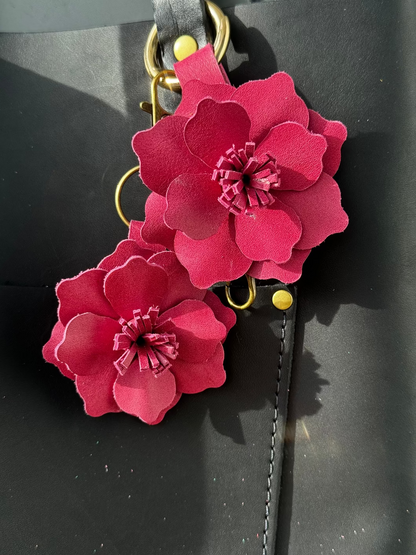 A small leather flower accessory in old rose color, attached to a black strap with a lobster clasp and a split ring, showing the texture and color of the leather.