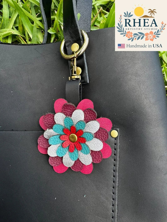 A multi-colored floral design leather purse charm accessory attached to a black bag with a metal clasp.