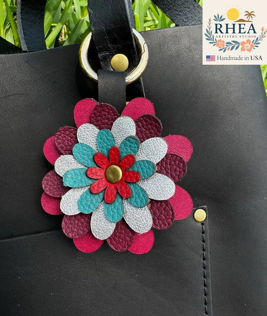 A multi-colored floral design leather leather bag charm accessory attached to a black bag with a metal clasp.