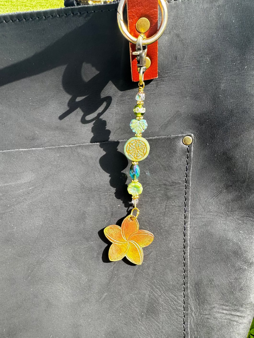 A handcrafted plumeria charm made with leather and solid brass hardware, featuring czech glass accents, attached to a keychain.