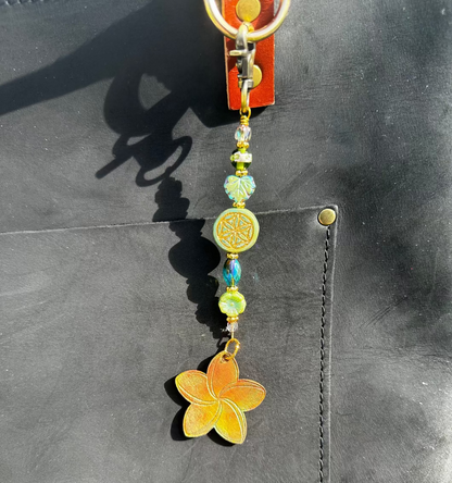 A handcrafted plumeria charm made with leather and solid brass hardware, featuring czech glass accents, attached to a keychain.