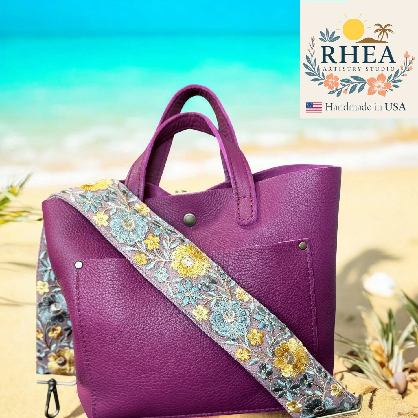 Purple handbag with floral purse strap on a beach background, featuring the RHEA Artisan Studio logo.