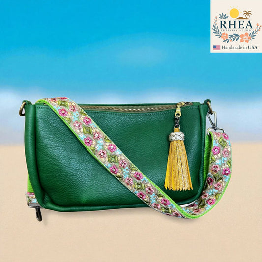 Green handbag with floral strap and yellow tassel on a blue and beige background, featuring the RHEA brand.