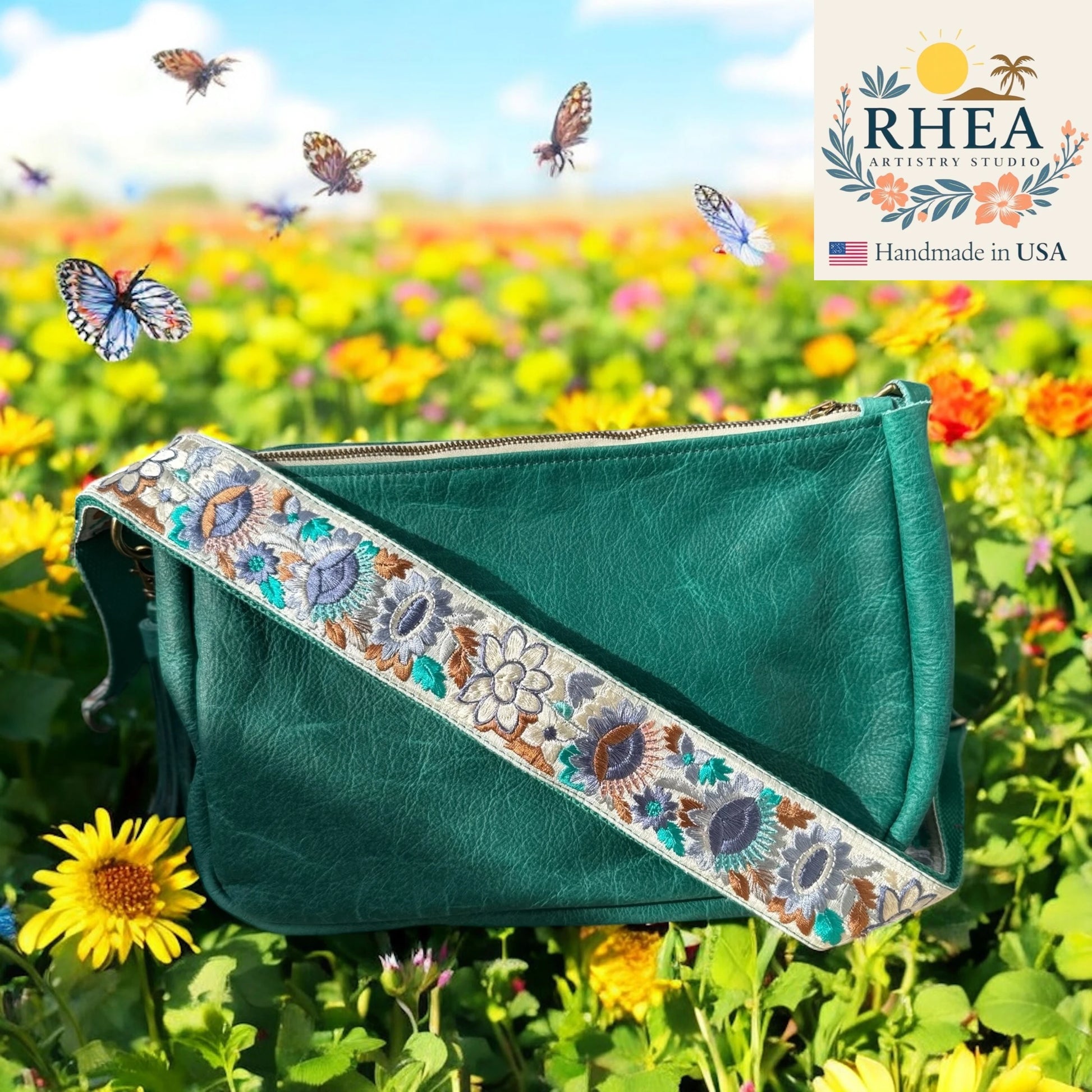 Green handbag with floral purse strap in a field of flowers and butterflies, featuring RHEEA Artistry Studio branding.