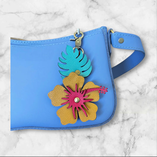 Mustard yellow hibiscus with red stamen , green leaf on a blue leather bag