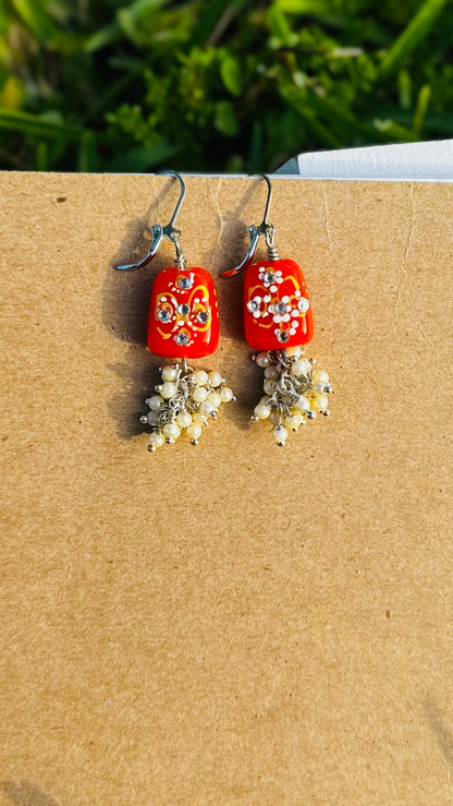Red earrings with floral designs and pearl-like beads on a old book