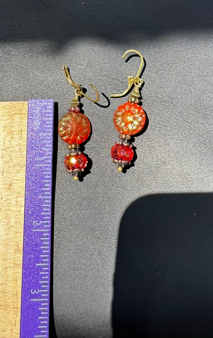 A pair of handcrafted Czech glass earrings with a serene glow, featuring a combination of rusty pink and brick orange hues, with brass hardware.