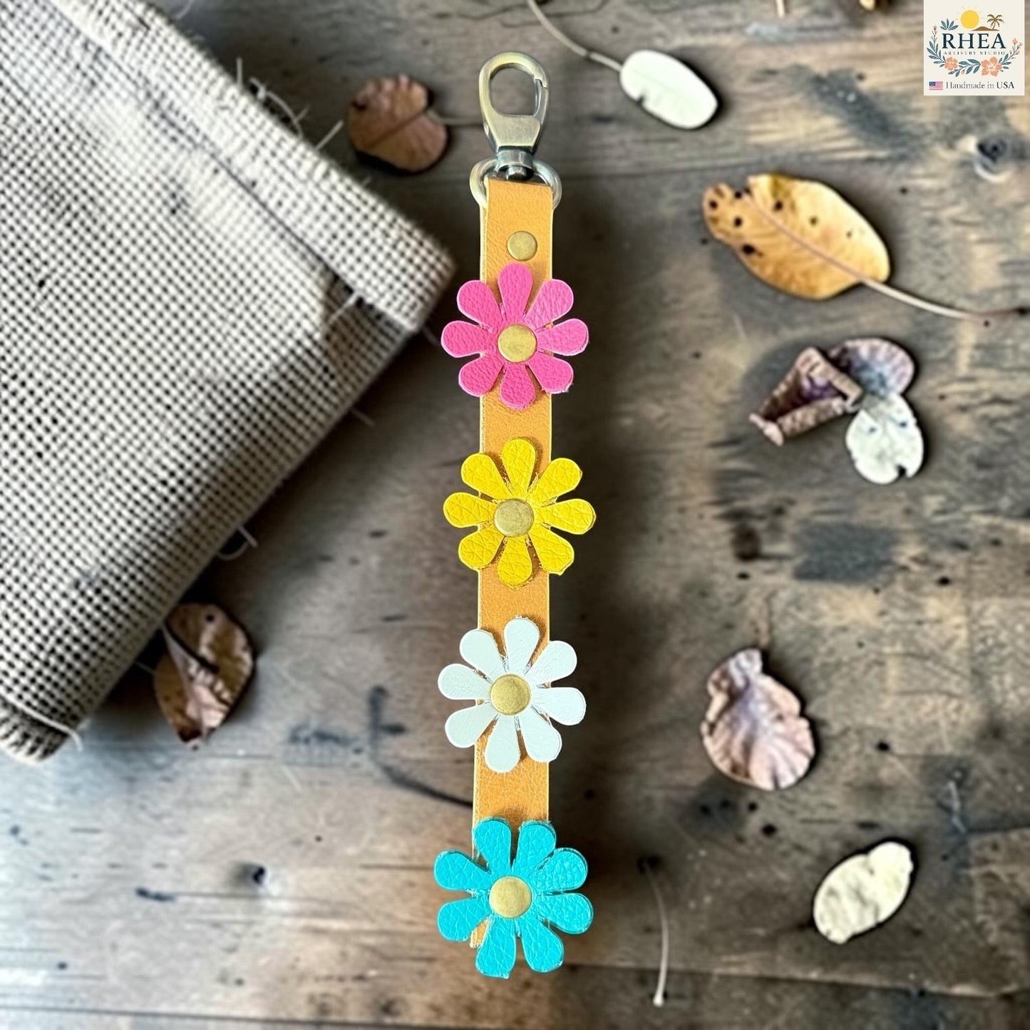 Rhea Artistry Studio handmade leather daisy wristlet keychain with pink, yellow, and blue flowers attached to a tan leather strap with brass rivets.