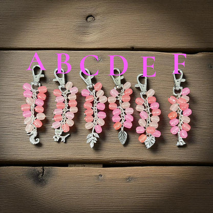Set of pink and silver keychains on a wooden surface with letters A to F above them.