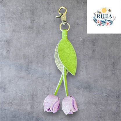 A handmade leather tulip charm with a green leaf and brown floral pattern, attached to a gold lobster clasp on a white marble surface.