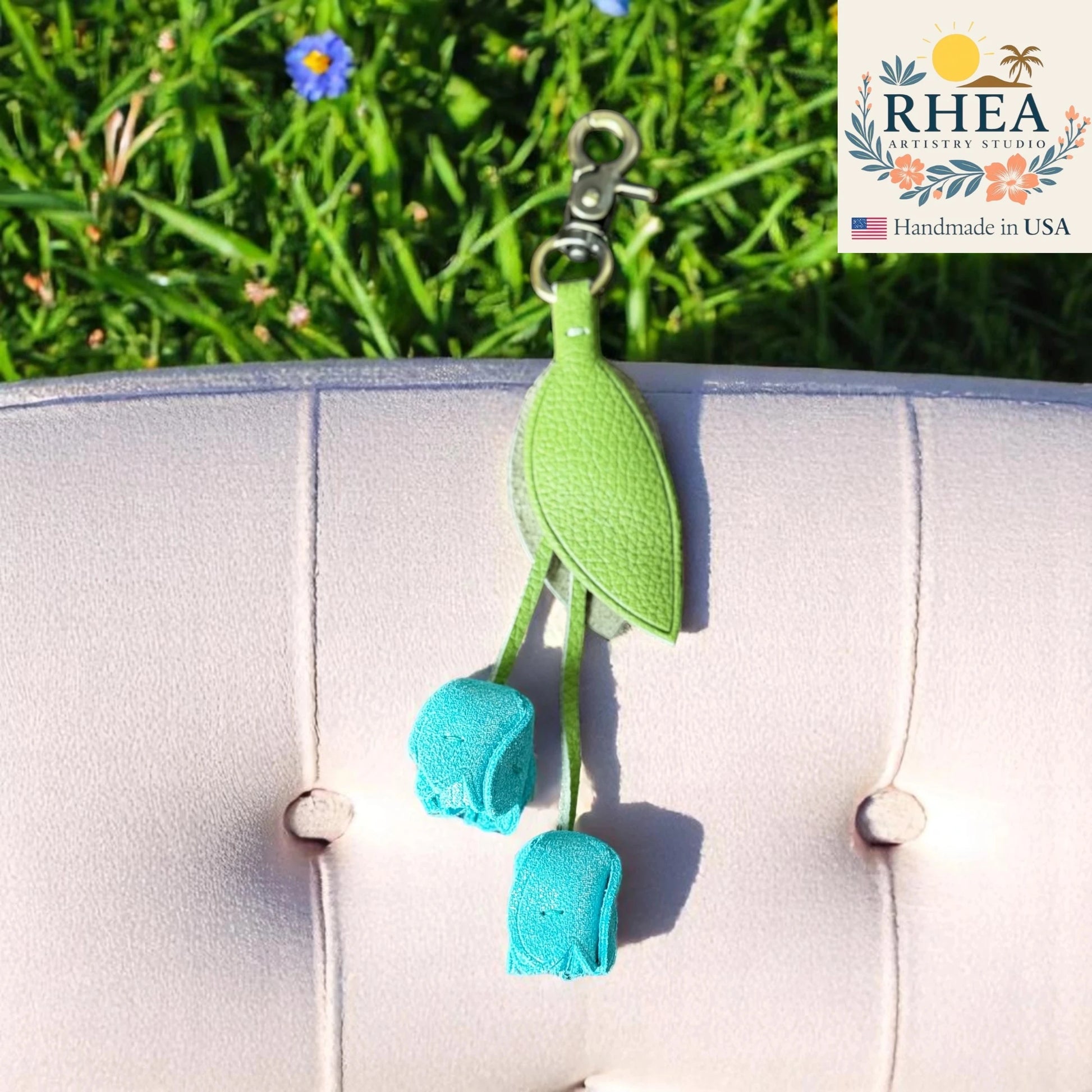 Green and blue leather purse charm with RHEA Artisan Studio branding on a grassy background