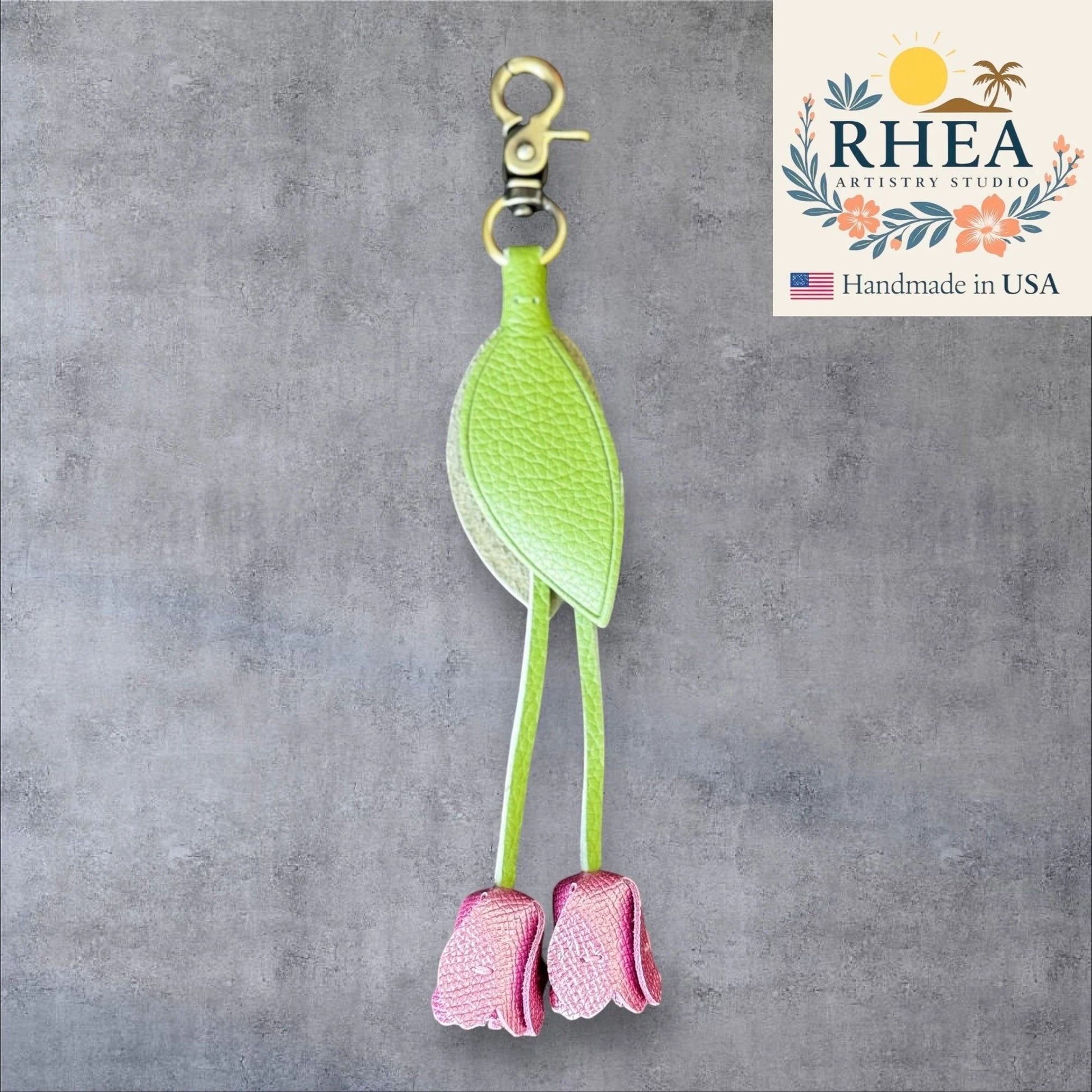 Green and pink leather purse charm with 'RHEA Artistry Studio' branding on a gray background