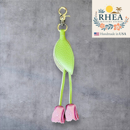 Green and pink leather purse charm with 'RHEA Artistry Studio' branding on a gray background