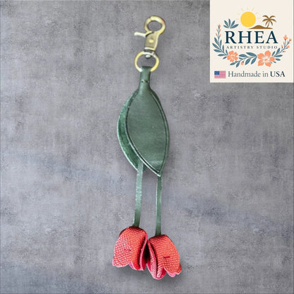 Green and red leather purse charm with RHEA Artistry Studio logo on a gray background