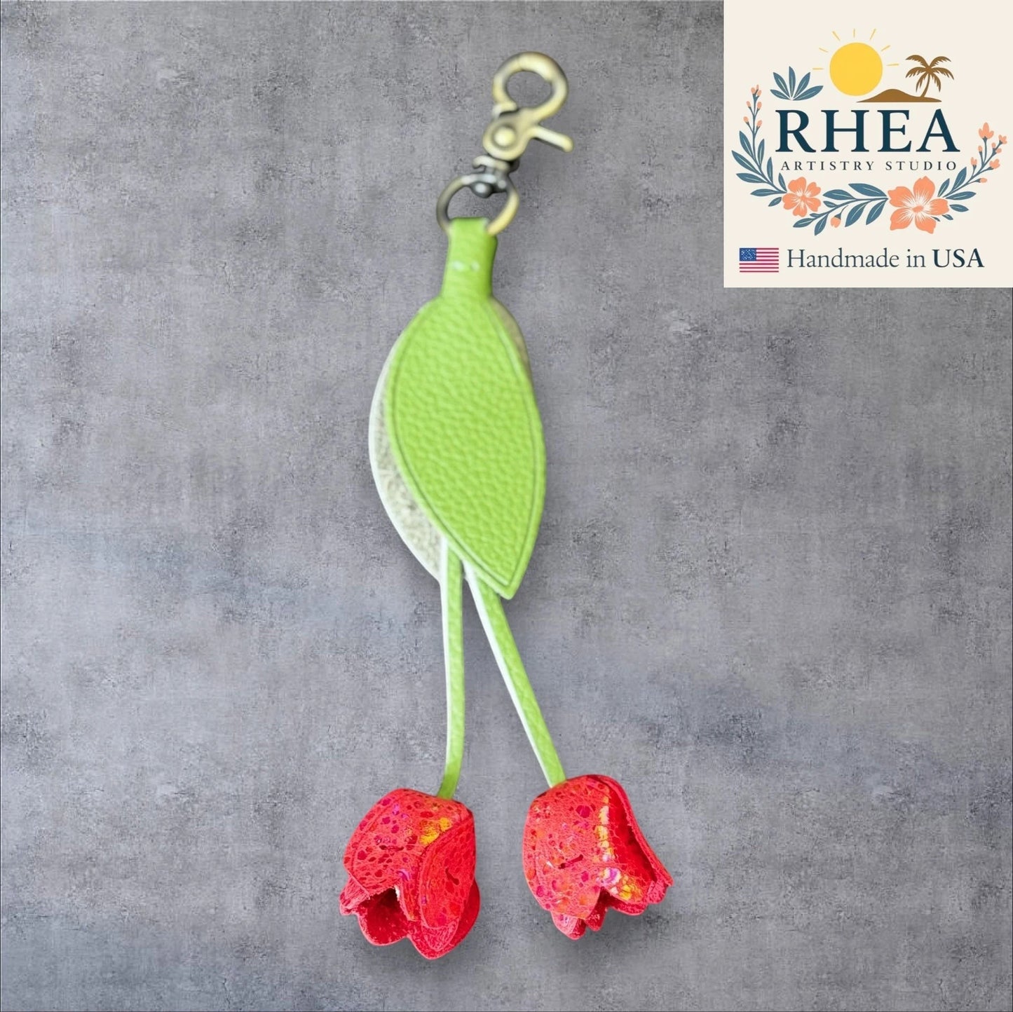 Green and red leather purse charm with 'RHEA Artistry Studio' logo on a gray background