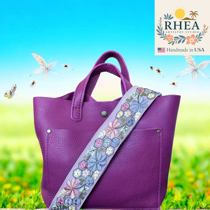 Purple handbag with a floral strap on a grassy background, featuring the RHEA Artistry Studio logo.
