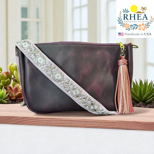 Purple handbag with luxury artisan strap and tassel on a wooden surface, RHEA brand visible.