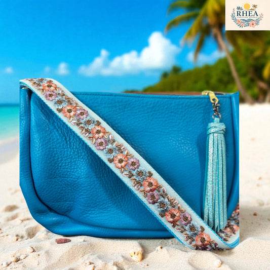Blue handbag with floral strap and tassel on a beach with palm trees in the background