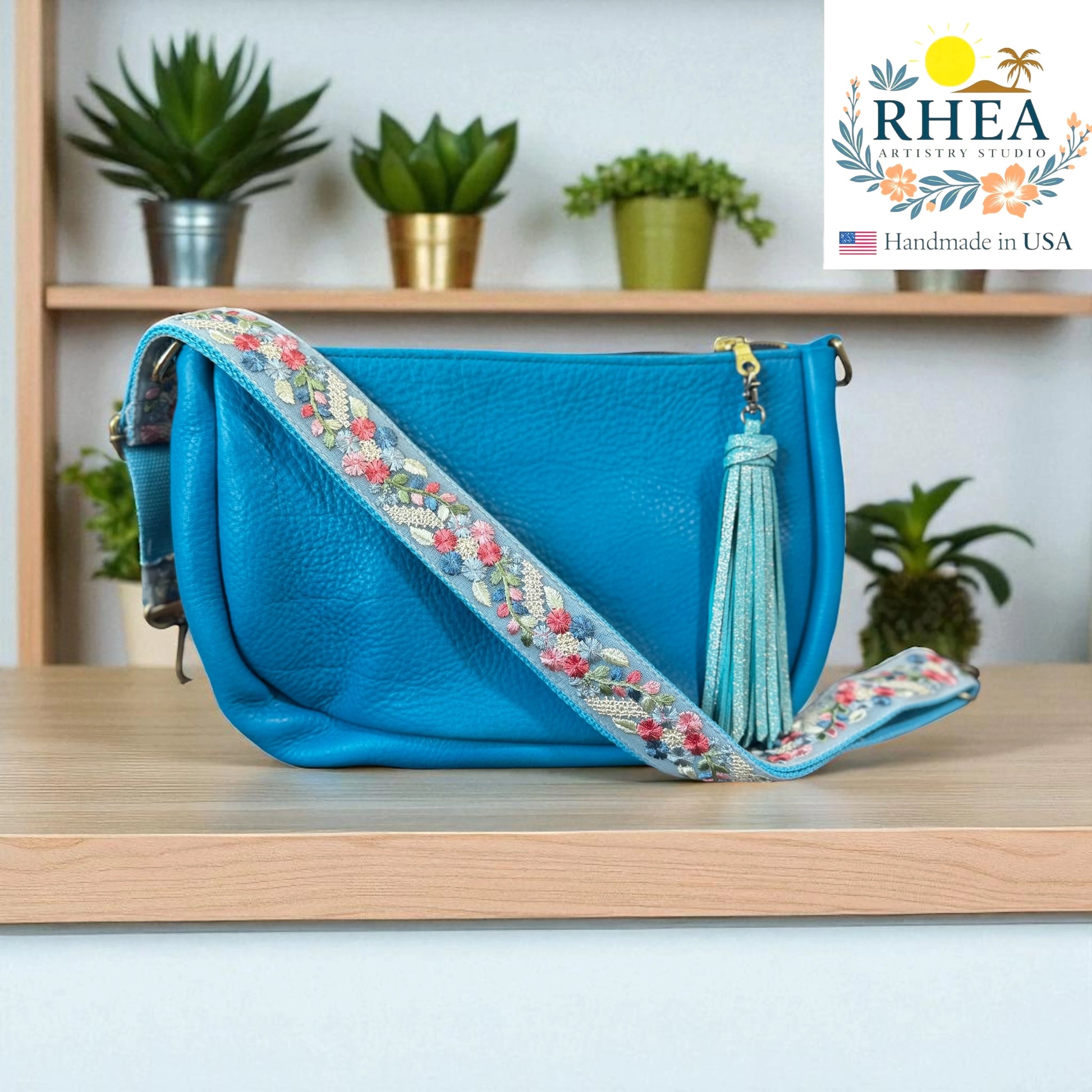 Blue handbag with floral  artisan bag strap on a wooden surface, RHEA brand visible