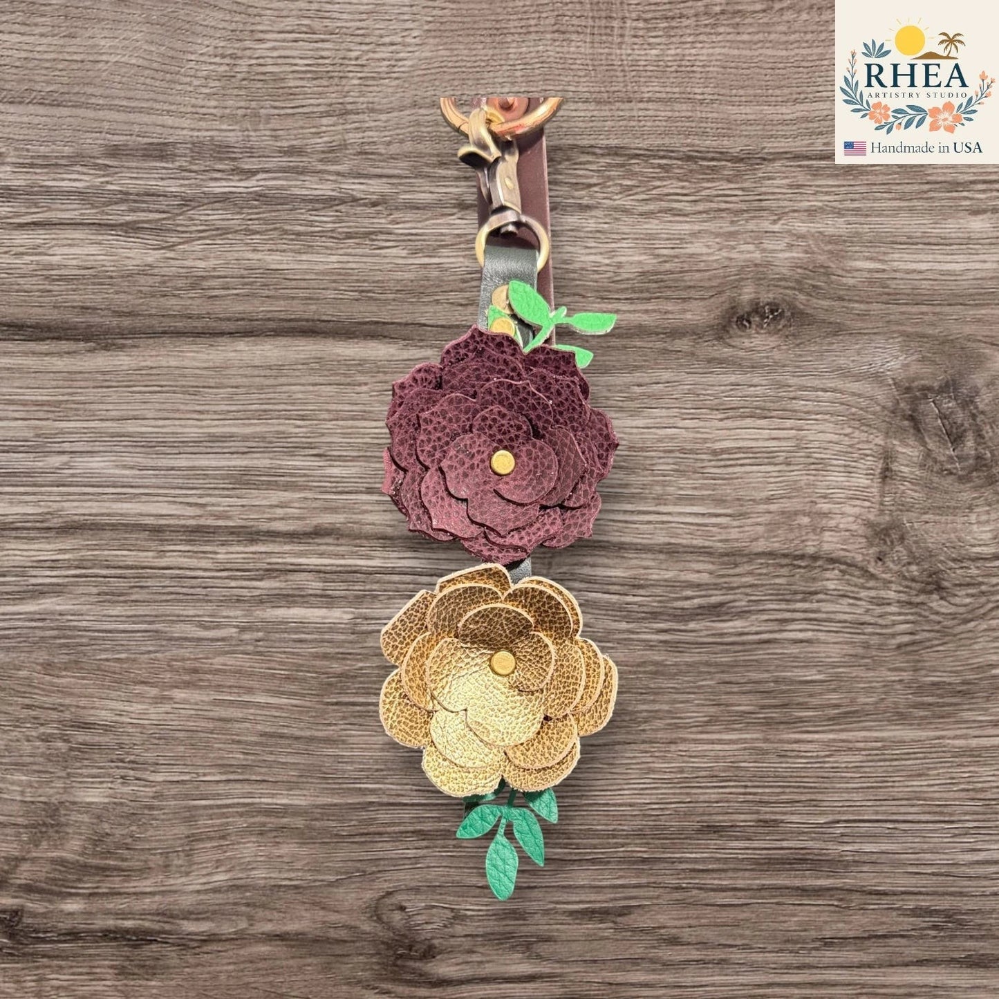 Floral keychain with purple and gold flowers on a wooden surface, featuring the RHEA brand.