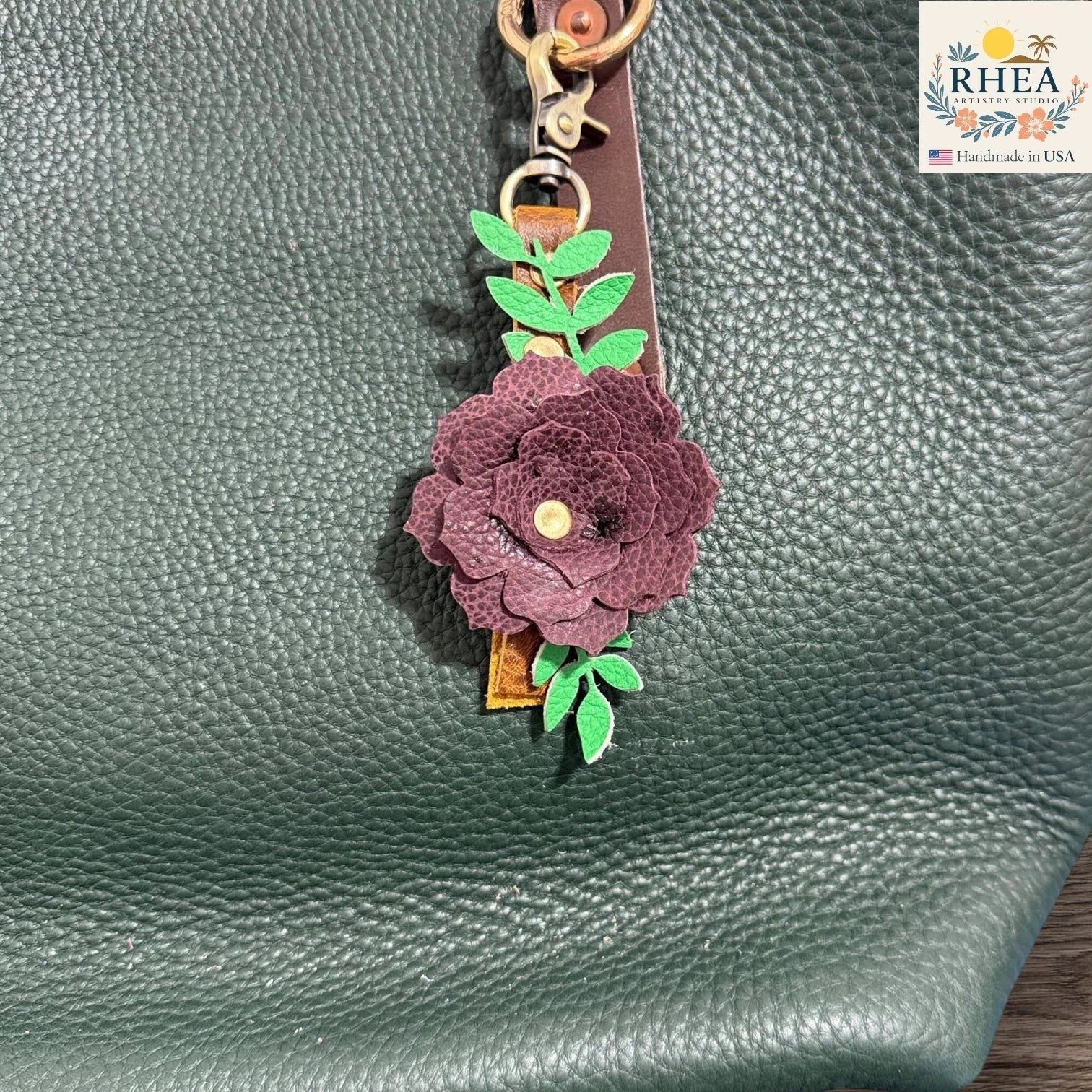 Floral keychain attached to a green textured surface with RHEA branding.