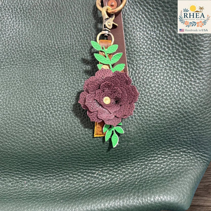 Floral keychain attached to a green textured surface with RHEA branding.