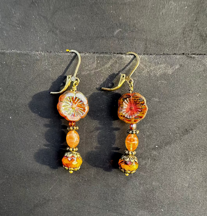 A pair of mustard yellow glass hibiscus flower drop earrings with brass accents placed on a dark surface.