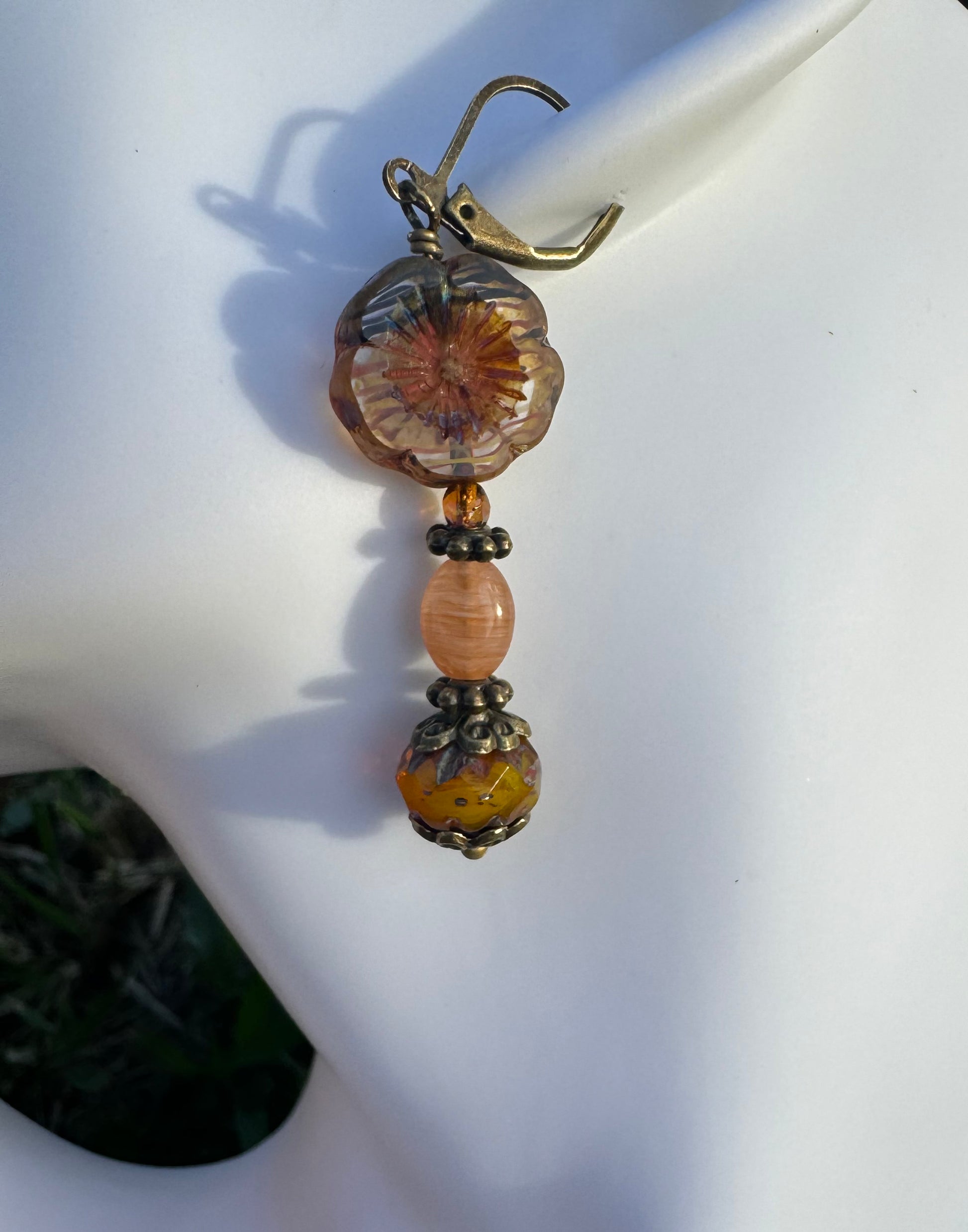 A pair of mustard yellow glass hibiscus flower drop earrings with brass accents placed on a model