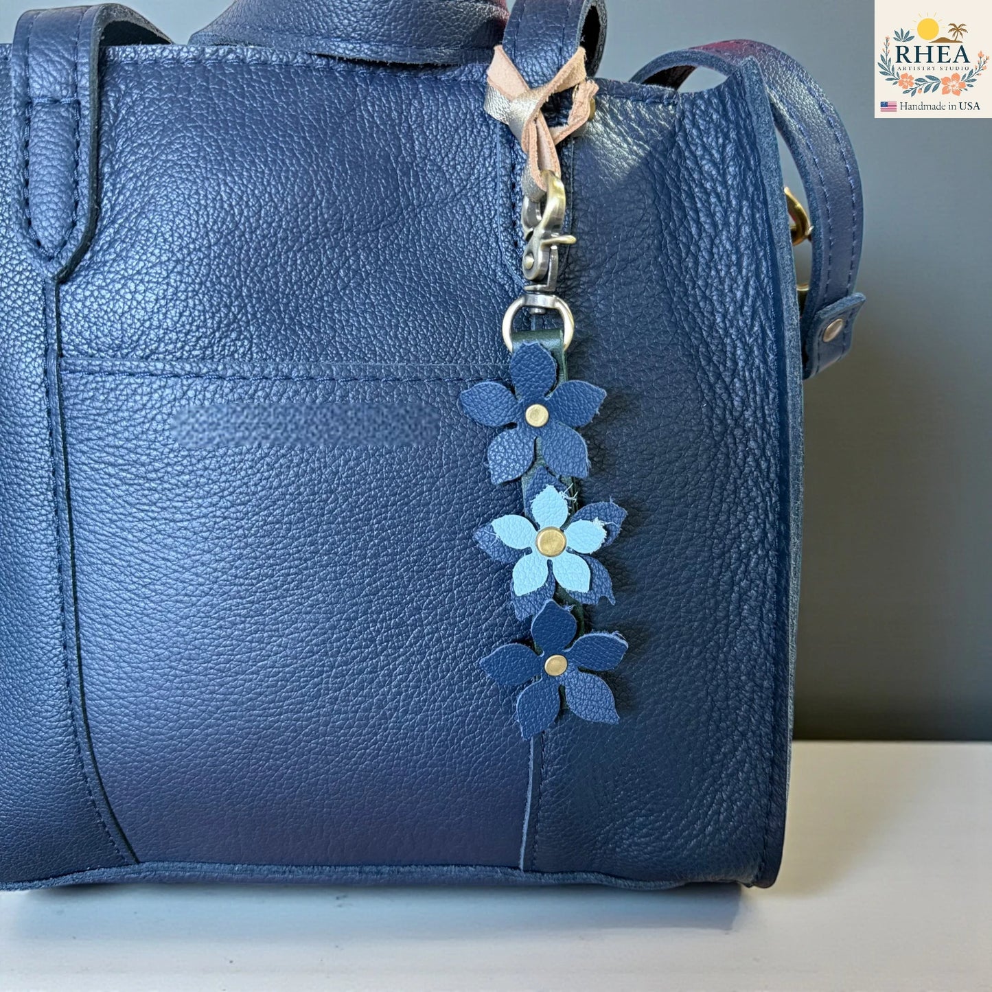 Blue leather handbag with a floral keychain charm on a neutral background
