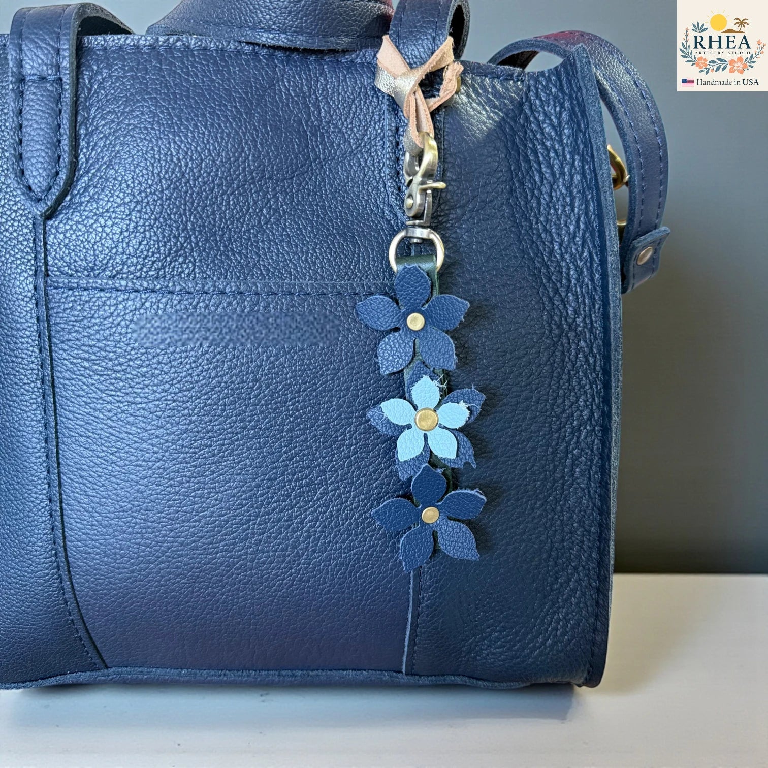 Blue leather handbag with a floral keychain charm on a neutral background