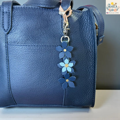 Blue leather handbag with a floral keychain charm on a neutral background